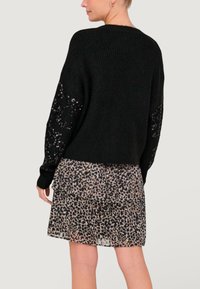 Pull noir en tricot avec des accents en sequins sur les manches, associé à une jupe à imprimé léopard en couches. Le pull a une coupe décontractée.