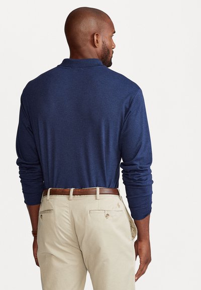 Navy poloshirt met lange mouwen, gemaakt van zachte stof, met een aansluitend ontwerp en een geribbelde kraag. Gecombineerd met lichtbeige chino's en een leren bruine riem.