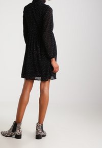 Black, dotted dress with a high neck, long sleeves, and a flared hem. Paired with black and white leopard-print ankle boots.