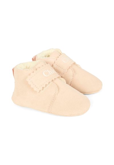 Jasnoróżowe zamszowe buciki dla niemowląt z miękką białą podszewką, falbaniastymi akcentami i rzepami ułatwiającymi zakładanie.