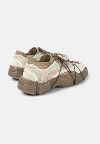 Beige ja ruskea lenkkari, jossa on verkkokangas yläosa, teksturoitu ruskea pohja ja ruskeat nauhat. Pohjassa on rosoinen kuvio, joka tarjoaa pitoa.