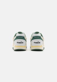 Sneaker verdi e bianchi con suola gialla, caratterizzati da pannelli in rete, perforazioni e un logo sul tallone. Dettaglio del colletto imbottito visibile.