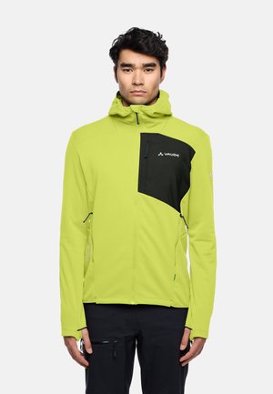 Limoengroene softshell jack met zwarte accenten op de borst, capuchon, ritszakken en reflecterende details. Lichtgewicht en getailleerd ontwerp.