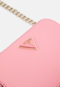 Růžová texturovaná kabelka s trojúhelníkovým zlatým a růžovým logo akcentem. Vybavená stříbrným řetízkem pro nošení.