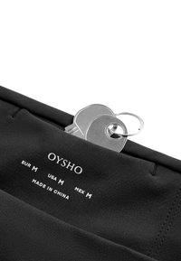 Étiquette de vêtement noire Oysho indiquant la taille medium pour l’Europe, les États-Unis et le Mexique avec un porte-clés en métal et deux clés insérées dans le tissu.