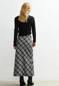 Czarny dziany sweter w połączeniu z długą spódnicą w kratę w odcieniach czerni, bieli i szarości. Modelka ma na sobie czarne botki na obcasie do kostki.