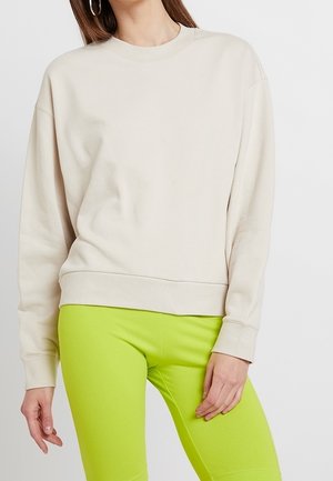 Sweatshirt beige avec un col rond et des coutures d'épaule tombantes, fabriqué en tissu doux. Associé à des leggings verts fluo, mettant en valeur le contraste.