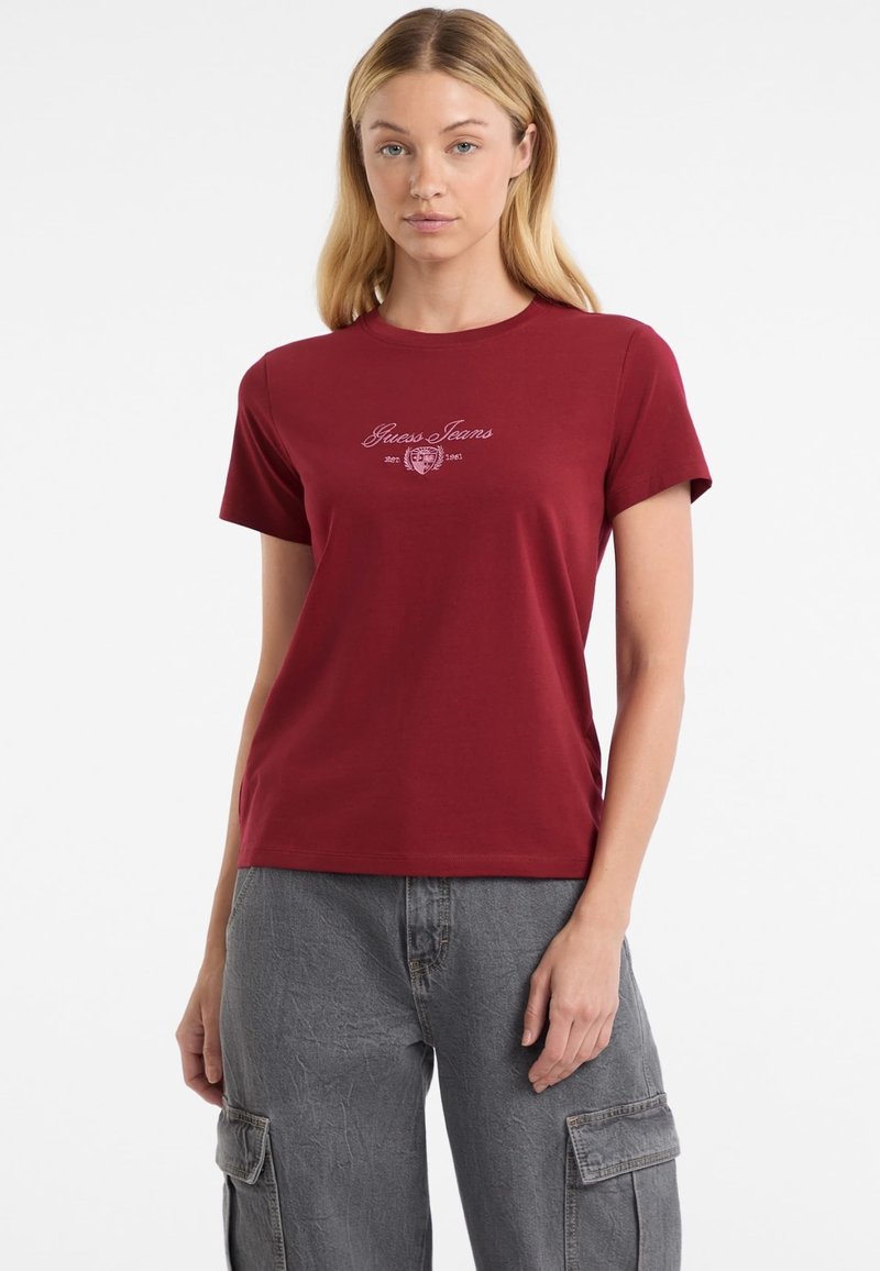 Červené bavlnené tričko s okrúhlym výstrihom a krátkymi rukávmi; na prednej strane je vyšívané logo "Guess Jeans" v kontrastnej farbe.