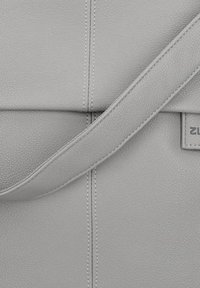 Bolso de cuero gris con un acabado texturizado, correa ajustable y costuras visibles, con una pequeña etiqueta en un lado.
