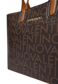 Brun læder tote taske med et præget mønster af navnet "Valentino" i guldskrift og beige accenter. Glat tekstur, struktureret form.