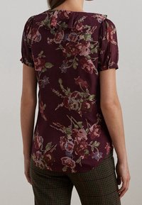 Mörkröd blus med korta puffärmar, volangkrage och en blandning av rosa, blå och gröna blommönster. Slät tygtextur.