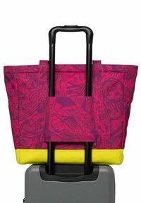 Grand sac fourre-tout rose avec des motifs géométriques vibrants, présentant des accents jaunes, conçu pour s'adapter sur les poignées de valise.