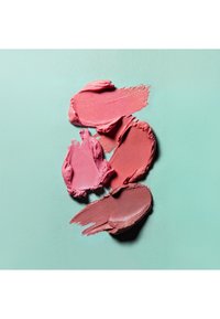 Läpprodukter i olika nyanser av rosa och rött, med krämiga texturer, applicerade i svepande drag på en slät mintgrön bakgrund.