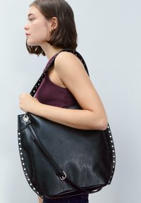 Borsa a spalla in pelle nera con accenti di borchie argentate lungo il bordo, dotata di una sola tracolla e di un design elegante e curvo.
