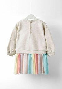 Hame dressi, jossa on beige yläosa pyöreällä pääntiellä ja kolme nappia takana, yhdistettynä monikerroksiseen hameeseen pastelliväreissä.