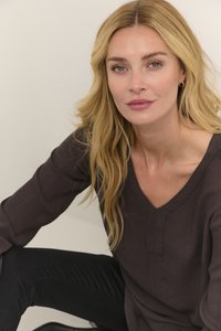 Haut V encolure en V texturé brun foncé avec des manches longues, associé à un jean foncé. Le mannequin a de longs cheveux blonds raides. Fond simple.