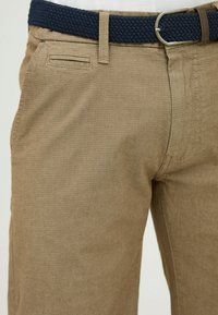 Beige trousers with a textured weave, featuring a navy braided belt and a small front pocket on the right side.
