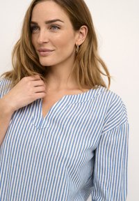 Sinine ja valge triibuline särk V-kaelusega, valmistatud kergest kangast, pikkade varrukatega ja pehme tekstuuriga.