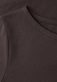 Primer plano de tela marrón que muestra costuras detalladas y un cuello redondo relajado de una prenda.