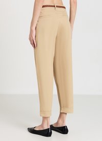 Pantaloni beige con una vestibilità rilassata, orlo a risvolto e cintura intrecciata marrone. Tessuto morbido con tasche posteriori e design su misura. Ballerine nere.