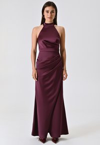 Bordeauxfarbene Satin-Halterkleid mit tailliertem Oberteil und drapierter Rockpartie. Verfügt über eine glatte Textur und einen seitlichen Schlitz, ergänzt durch elegante rote Schuhe.