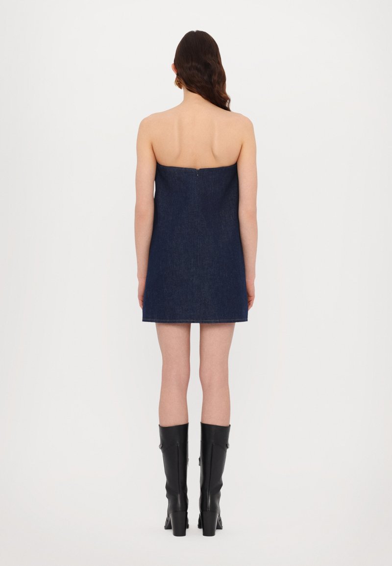 Denim strapless jurk in donkerblauw met een gladde textuur, voorzien van een aansluitende buste en een rechte silhout, gecombineerd met hoge zwarte laarzen.