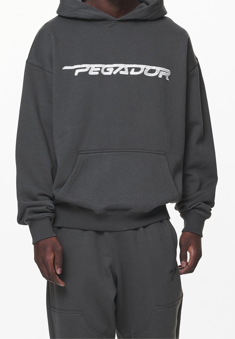 Grå huvtröja med en framficka, ribbade muddar och nederkant. Har en vit broderad "PEGADOR"-logotyp över bröstet.