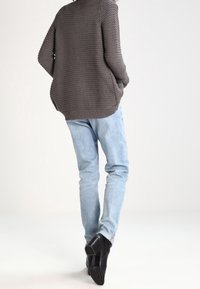 Gray ribbed oversized sweater, light blue slim-fit jeans, and black heeled ankle boots shown from the back against a neutral background.