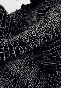 Tissu noir avec un motif de grille blanche, présentant des épaisseurs de lignes variées. La texture semble douce et tricotée, tombant le long du bras.