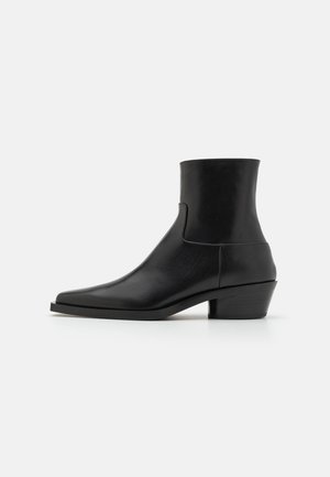 Černá kožená kotníková bota se čtveratou špičkou, matným povrchem a nízkým block podpatkem. Nabízí hladký, elegantní design bez zdobení.