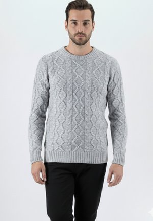 Suéter gris de punto con patrones de trenza, cuello redondo y puños acanalados. Se lleva sobre pantalones oscuros, mostrando un diseño texturizado.