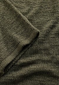 Material tricot verde măsliniu cu un model texturat, cu țesătură deschisă și o margine pliată vizibilă în colțul din stânga sus.