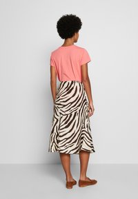 Coral short-sleeve t-shirt paired with a long, tiered skirt featuring a brown and cream zebra stripe pattern and brown slip-on shoes.