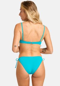 Tyrkysové bikiny so nastaviteľnými ramienkami, hladkou textúrou, minimalistickým dizajnom a detailmi s viazaním na spodnej časti. Logo značky viditeľné na zadnej strane.
