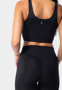 Top corto deportivo negro y leggins, textura suave, diseño ajustado, cinturilla de altura media, con un pequeño logo en la parte trasera del top.