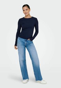 Top de manga larga azul marino combinado con jeans de pierna ancha azul claro, que presentan acentos desgastados y dobladillos deshilachados, usado con zapatillas blancas.