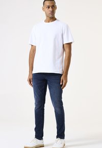 Witte katoenen t-shirt met korte mouwen, gecombineerd met donkere denim jeans en witte sneakers met textuurelementen en een gumrubberen zool.