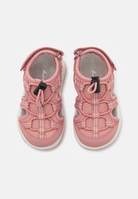 Rozā sieta sandales ar teksturētu augšdaļu, elastīgām šņorēm un ar rāvējslēdzēju. Iespējas ietver baltas akcentus un mīkstinātu zoli ar noapaļotu formu.