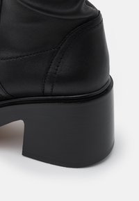 Bottine en cuir noir à bout arrondi, dotée d'un talon épais et chunky, avec des détails de couture visibles le long des coutures.