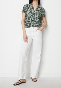 Blouse légère verte à pois noirs, col en V et manches courtes, associée à un jean blanc droit et des sandales noires à brides.