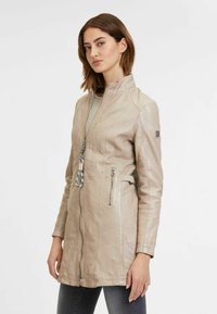 Beige leren jack met een hoge kraag, een voorrits, twee zijzakken met rits en een verstelbare taille. Glad textuur en minimalistisch ontwerp.