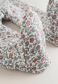 Kukkatulosteinen kangastuote, jossa on pieniä punaisia, sinisiä ja vihreitä kukkia valkoista taustaa vasten; pehmeä, pehmustettu rakenne.