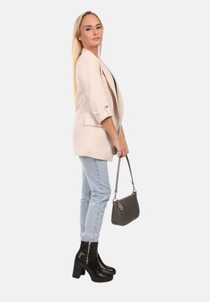 Blazer beige avec manches retroussées, jean skinny bleu clair, et bottes noires à plateforme hautes. Sac à main gris avec bandoulière.