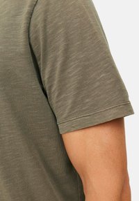 Olijfgroene katoenen t-shirt met een klassieke pasvorm, korte mouwen en een ronde hals. De stof heeft een subtiel gestructureerd patroon.