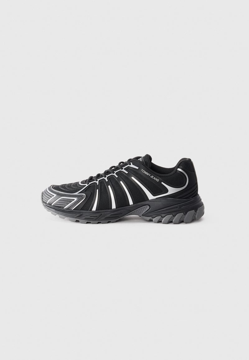 Scarpa sportiva nera con dettagli bianchi, caratterizzata da una tomaia testurizzata, un design curvo e una suola in gomma con battistrada prominente per una migliore aderenza.