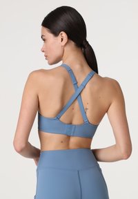 Top sportivo blu con spalline incrociate e chiusura posteriore a gancio. Tessuto liscio, design minimalista, presenta un piccolo logo sul retro.