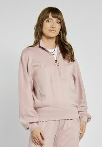 Jasnoróżowy sweatshirt z półzamkiem, ściągaczem na dole i miękkim materiałem. Posiada przednią kieszeń oraz szerokie rękawy dla luźnego kroju.