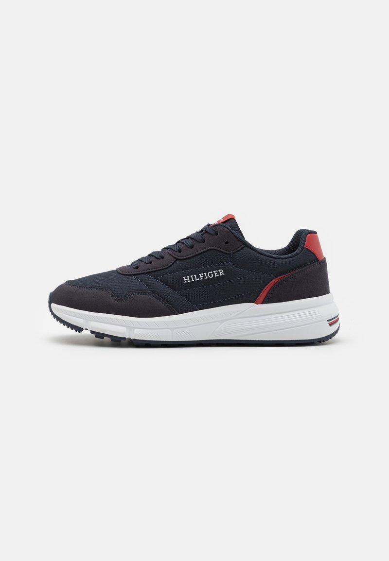 Navy blue athletic sneakers with a fabric upper, white midsole, red heel accents, and brand logo on the side. Textured rubber outsole.