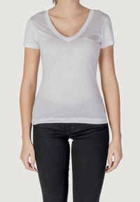 T-shirt blanc à manches courtes et col en V, en tissu léger, avec un logo discret sur le côté gauche de la poitrine et une coupe ajustée.