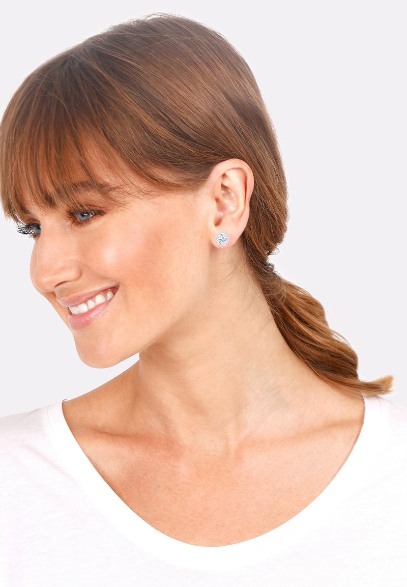 Orecchini rotondi in argento con superficie texture, caratterizzati da un design floreale. Chi li indossa ha i capelli castano chiaro ed è vestita con una maglietta bianca.
